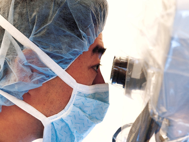 Person in surgical protective equipment looking through microscope eyepieces
