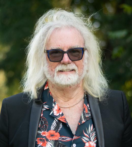 Older man with long white hair and beard wearing sunglasses and floral shirt outdoors