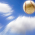 A baseball in motion against a bright blue sky with white clouds, appearing blurred to show speed.